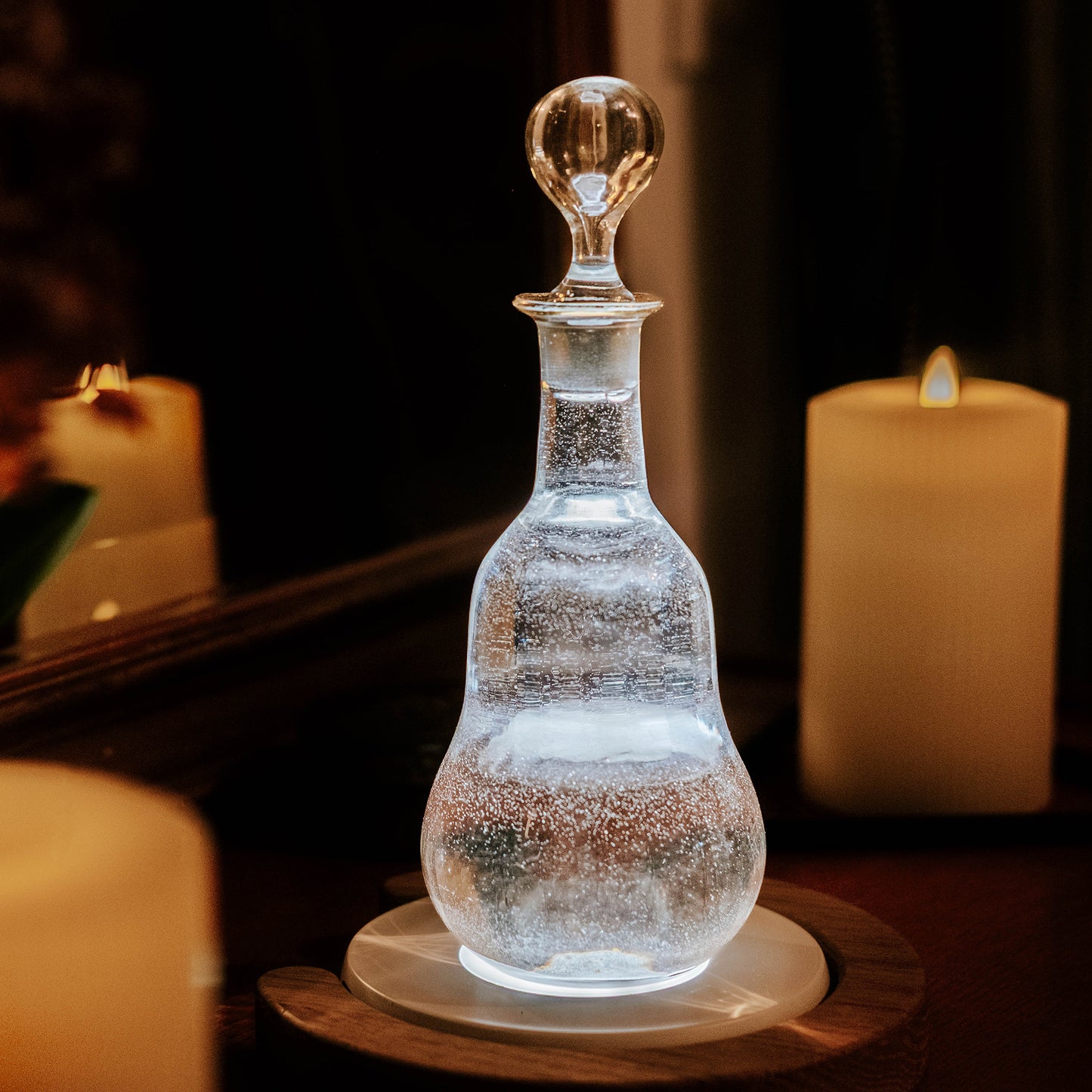 Carafe ancienne éclairée avec dessous de carafe lumineux Yobe light dans décor à la bougie devant miroir avec anneau en chêne yobe ring around