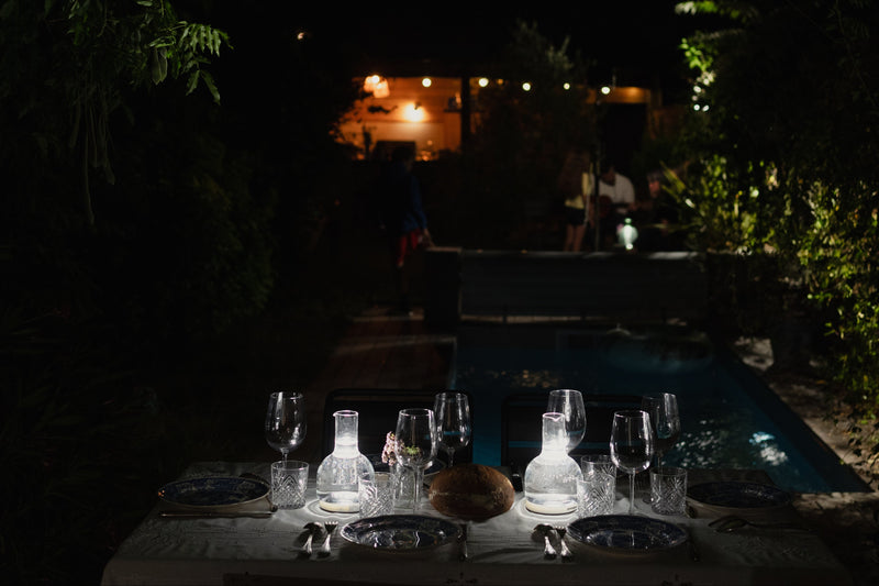 table vintage avec verres à vin deux carafes lumineuses posées sur supports lumineux dans un cadre exterieur au bord d'une piscine 