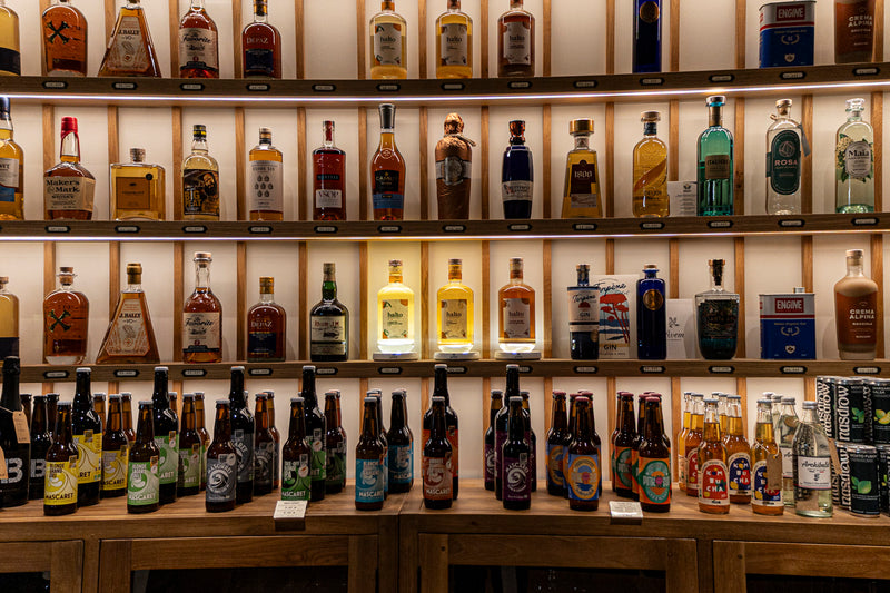 linéaire de bouteilles posées sur des étagéres en bois. Trois bouteilles au centre sont éclairées par des supports lumineux individuels 