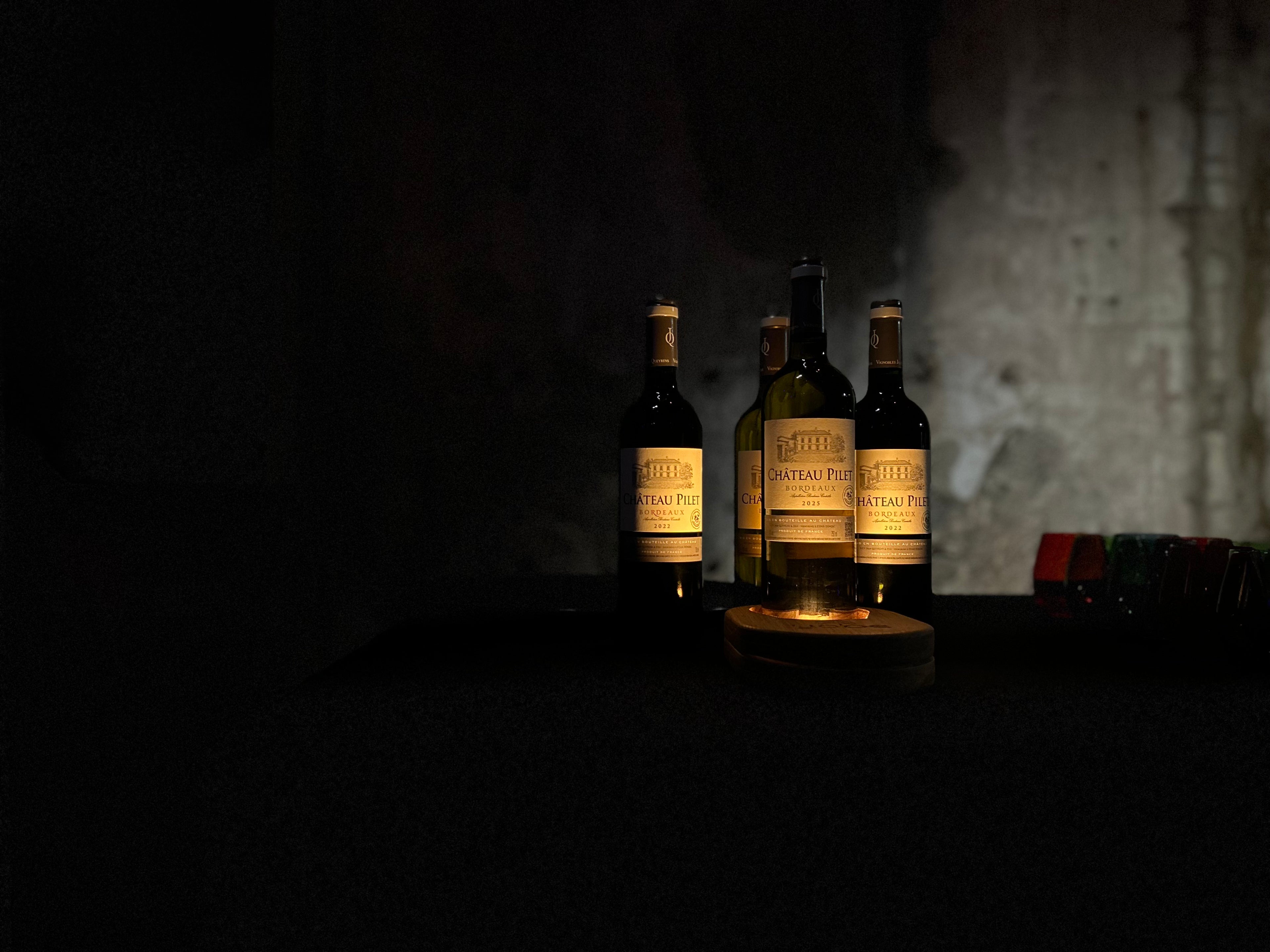 quatre bouteilles de chateau pillet illuminée par un support en bois yobe beam light dans un décor sombre minimaliste 