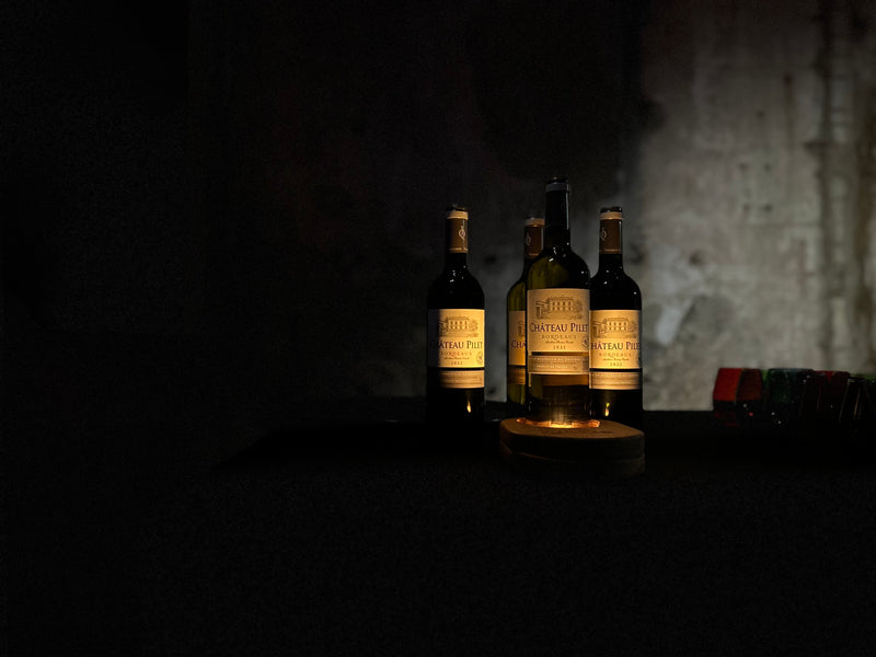 quatre bouteilles de chateau pillet illuminée par un support en bois yobe beam light dans un décor sombre minimaliste 