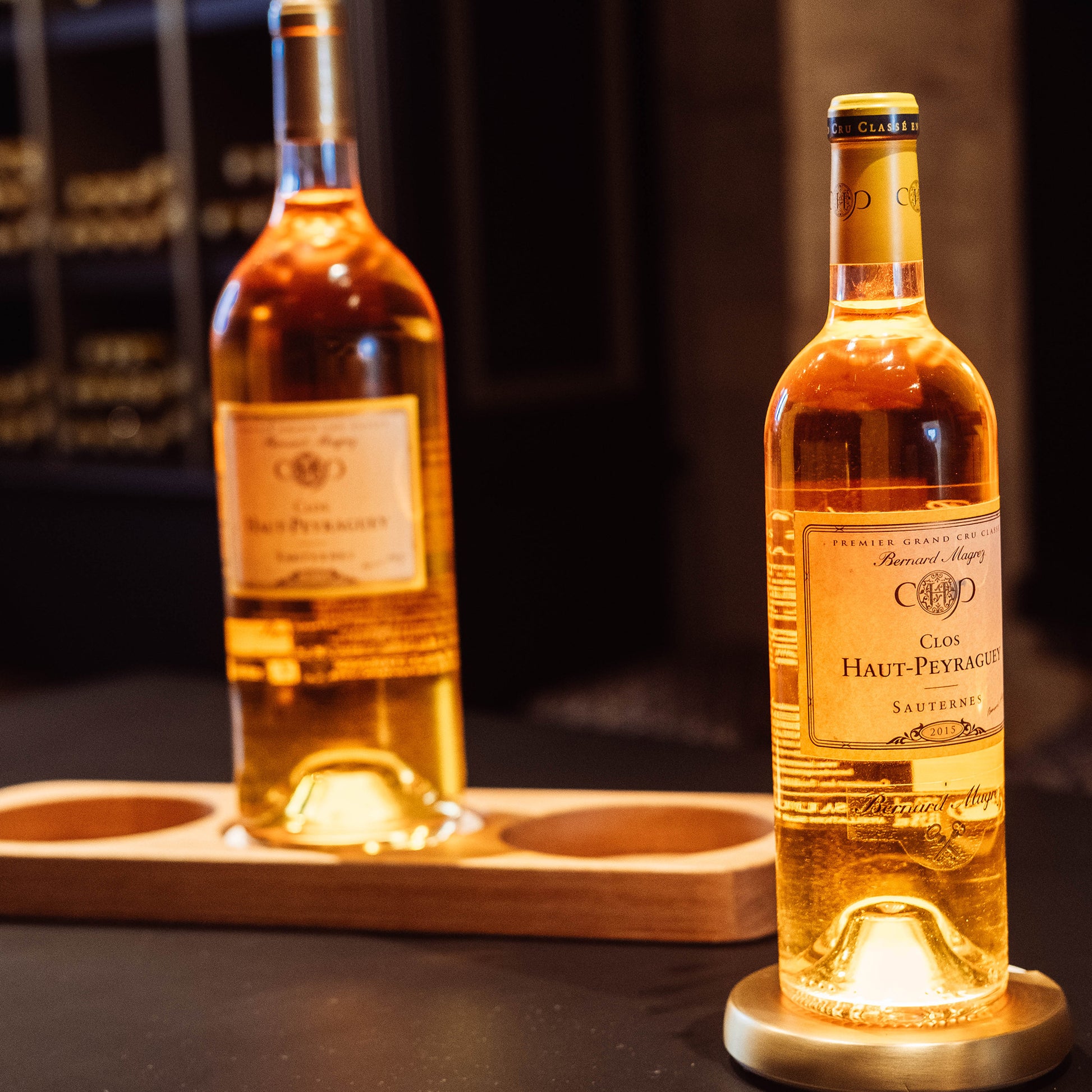 au premier plan bouteille de sauternes clos haut Peyraguet illuminé par support yobe light pro recouvert d'une coque dorée - au second plan magnum clos haut peyraguet éclairé par dessous de bouteille lumineux yobe light Pro 